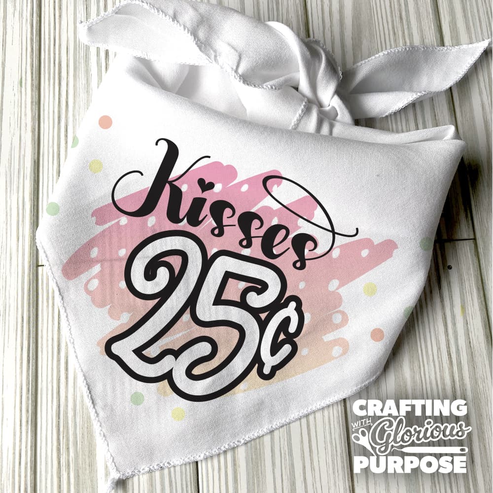 White bandana with 'Kisses 25 cents' text on a wooden surface, featuring the brand 'Crafting with Glorious Purpose'.
