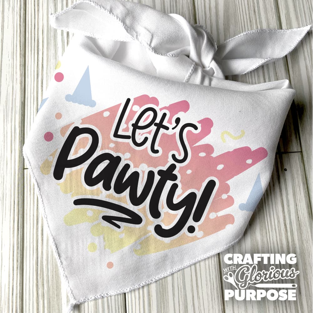 White bandana with 'Let's Pawty!' text and colorful design on a wooden surface, featuring the brand 'Crafting with Glorious Purpose'.