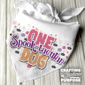 White bandana with 'ONE Spook-tacular Dog' text and Halloween-themed design on a wooden surface.
