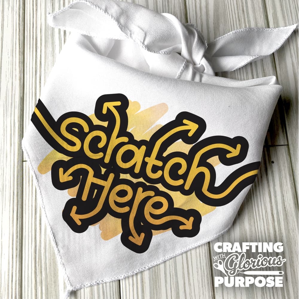 White bandana with 'Scratch Here' text in gold and black on a wooden surface, featuring the brand 'Crafting with Glorious Purpose'.