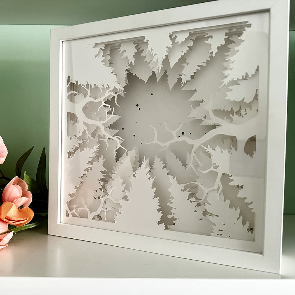 Framed decorative wall art with tree silhouette design on a light surface.