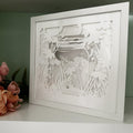 Framed paper cutout art of a jar with flowers and a butterfly on a white surface.