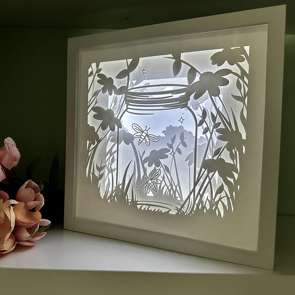 Framed paper cut art of a jar with flowers and butterflies on a dark background