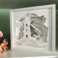 White paper sculpture of a lighthouse with waves and clouds, framed against a green background.