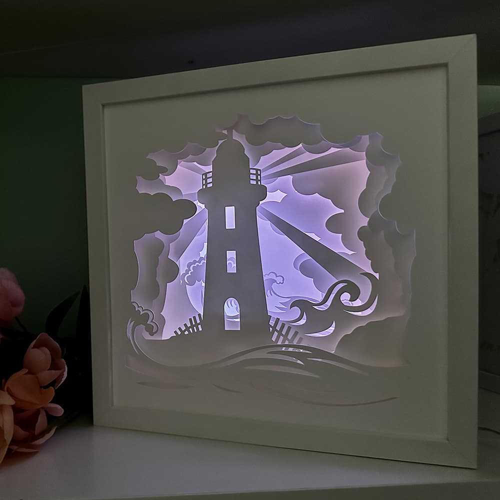 Framed paper cutout of a lighthouse with a purple glow on a dark background