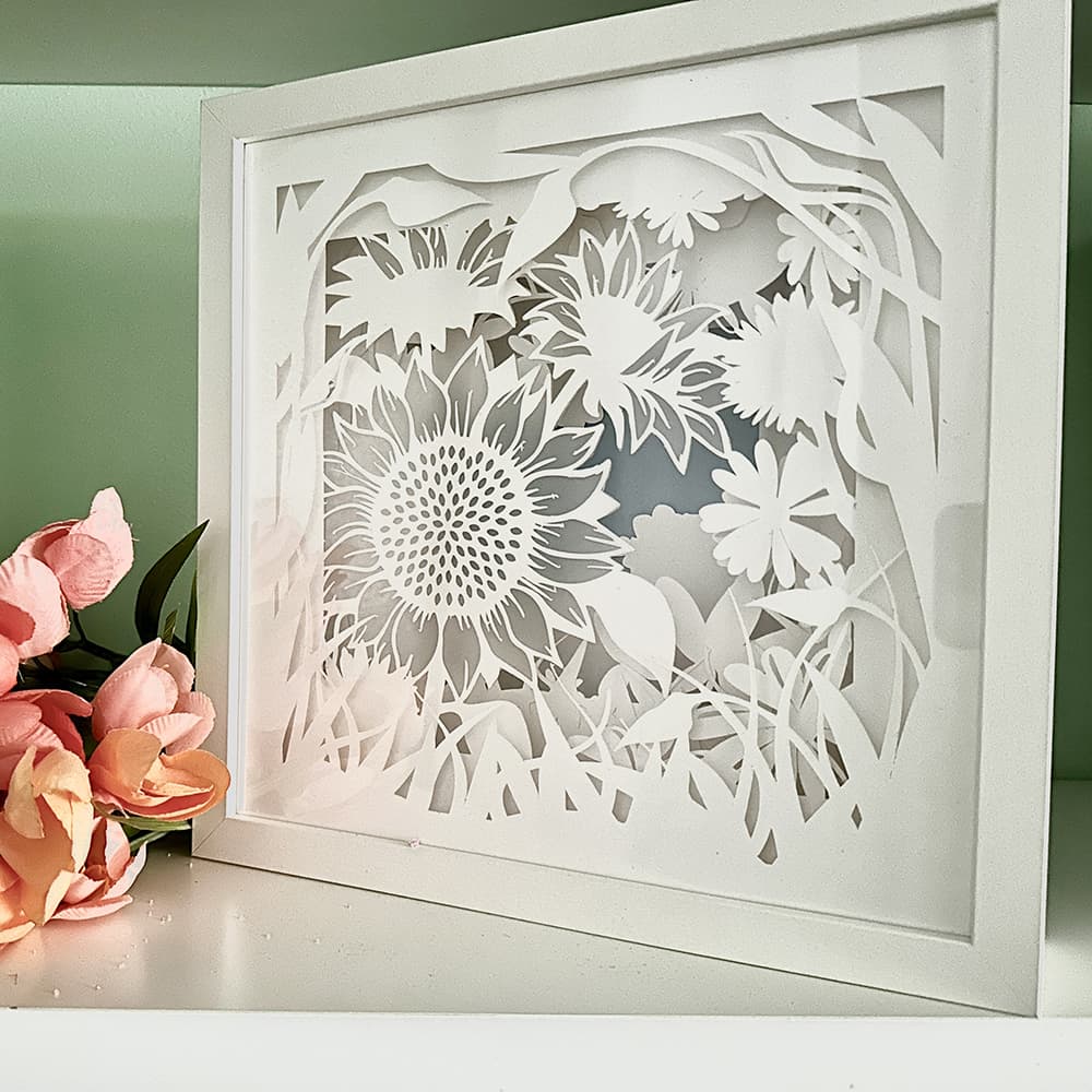 Framed paper cutout of sunflower design with pink flowers on a light green background
