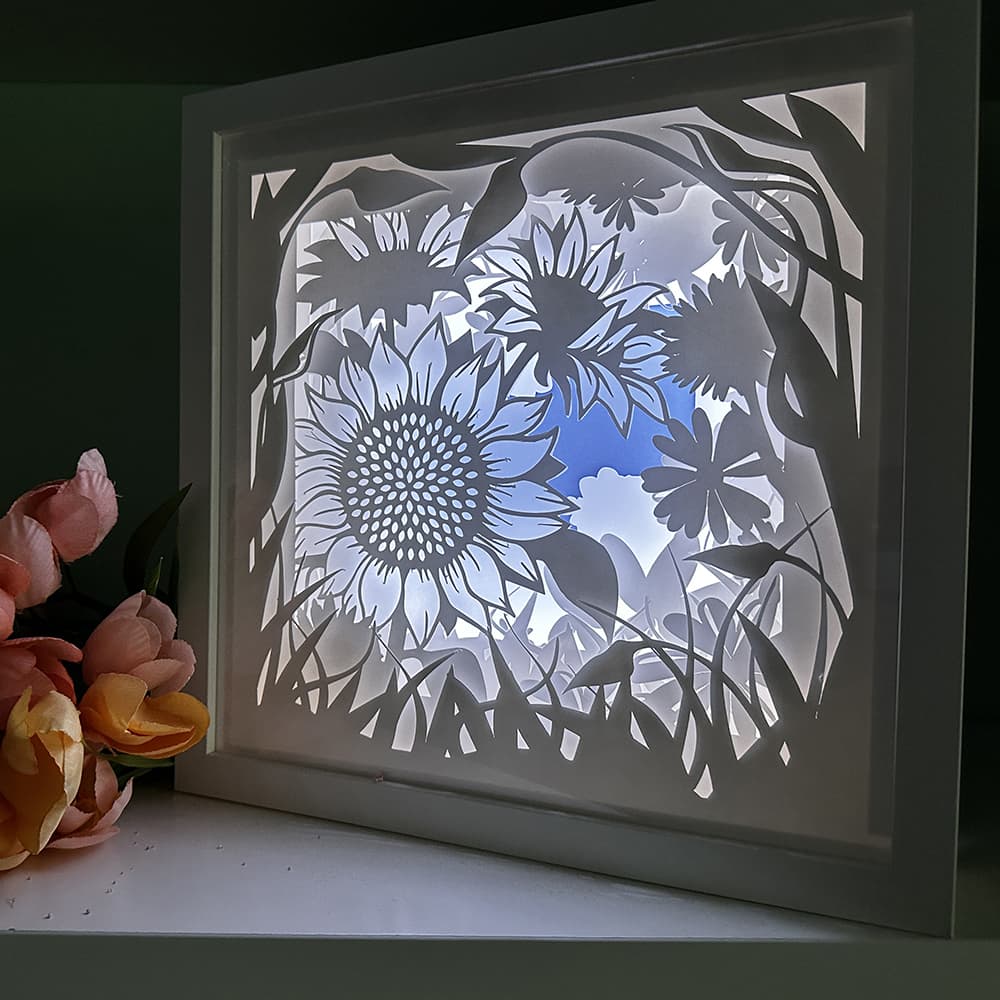 Framed paper cutout of floral design with sunflowers and leaves on a dark background