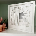 Framed paper cut art of a tropical scene with palm trees and a beach.