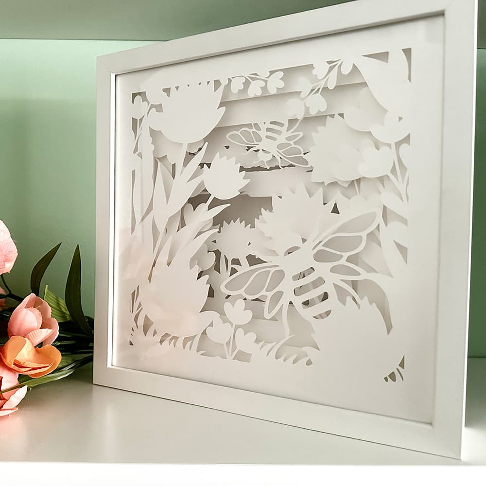 Framed paper art with floral and bee design on a light green background