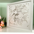 Framed paper art with floral and bee design on a light green background