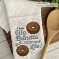 White towel with 'I like Big Bundts and I Cannot Lie!' text and bundt cake illustrations on a wooden surface with a wooden spoon.