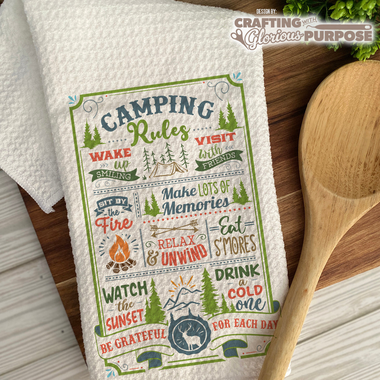 Camping-themed towel with text and graphics on a wooden surface with a wooden spoon.