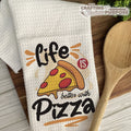 Dish towel with pizza design and text 'Life is better with Pizza' on a wooden surface with a wooden spoon.