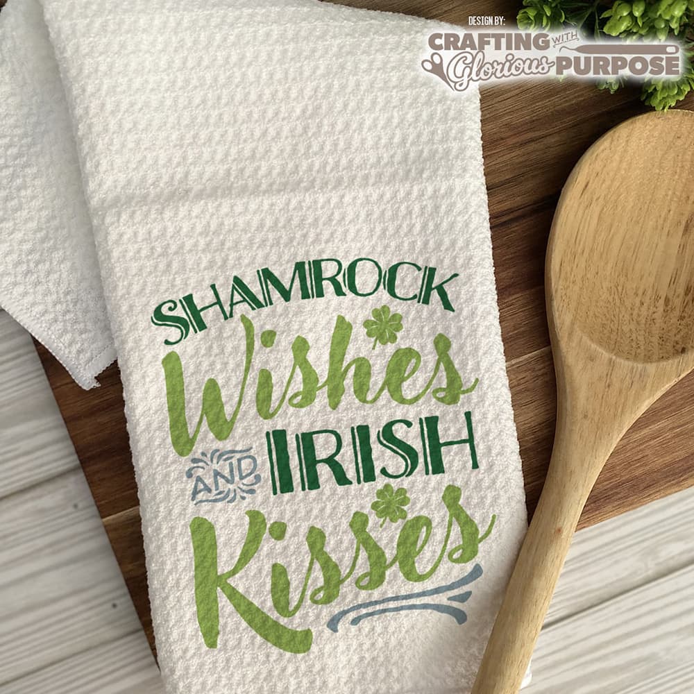 White towel with 'Shamrock Wishes and Irish Kisses' text on a wooden surface with a wooden spoon.
