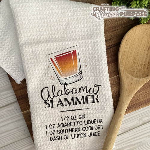 Dish towel with 'Alabama Slammer' recipe on a wooden surface with a wooden spoon.