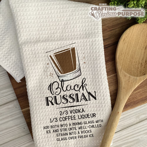 White towel with Black Russian cocktail recipe on a wooden surface with a wooden spoon.