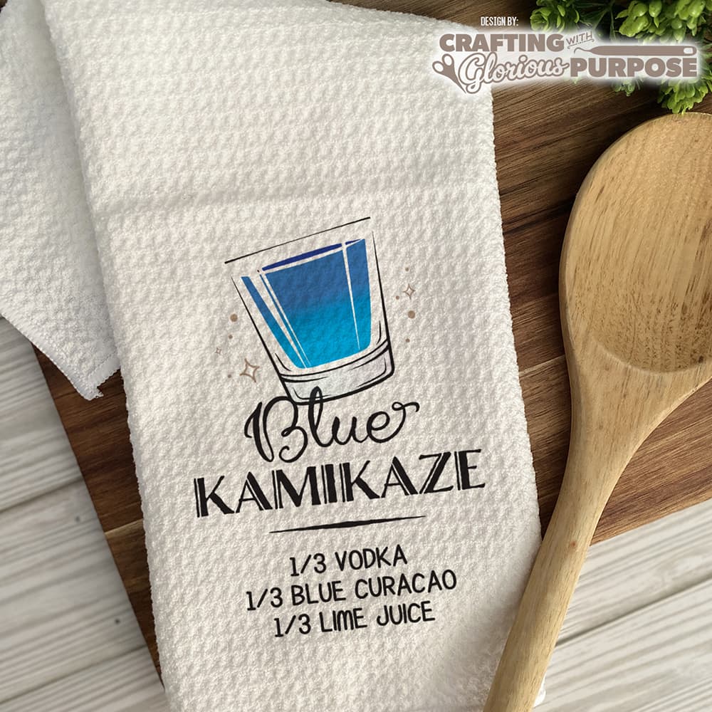 White towel with Blue Kamaikaze recipe graphic on a wooden surface with a wooden spoon.