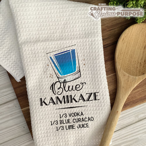 White towel with Blue Kamaikaze recipe graphic on a wooden surface with a wooden spoon.