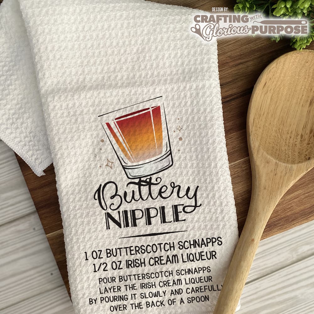 White towel with 'Buttery Nipple' recipe graphic and wooden spoon on a wooden surface.