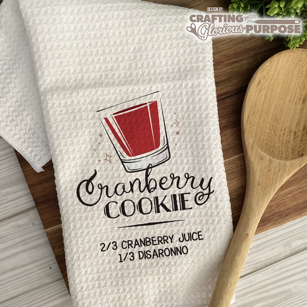 White towel with cranberry cookie recipe graphic on a wooden surface with a wooden spoon.