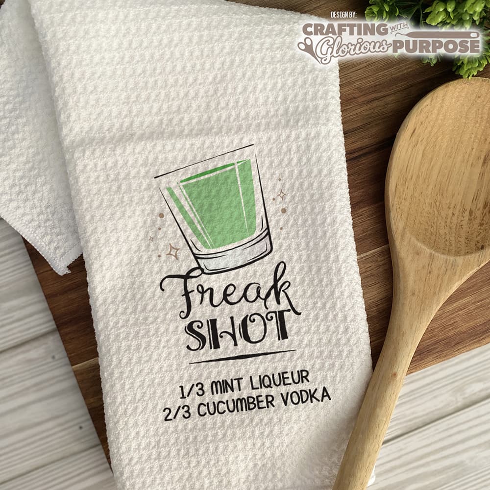 White towel with 'Freak Shot' graphic and text, wooden spoon on a wooden surface