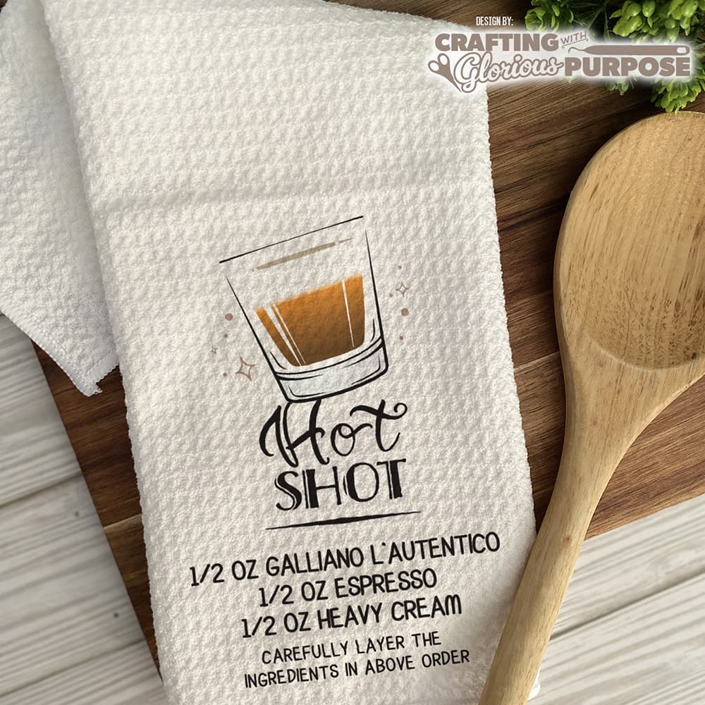 White towel with 'Hot Shot' recipe graphic and wooden spoon on a wooden surface
