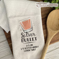 White towel with 'Silver Bullet' cocktail recipe graphic and wooden spoon on a wooden surface.