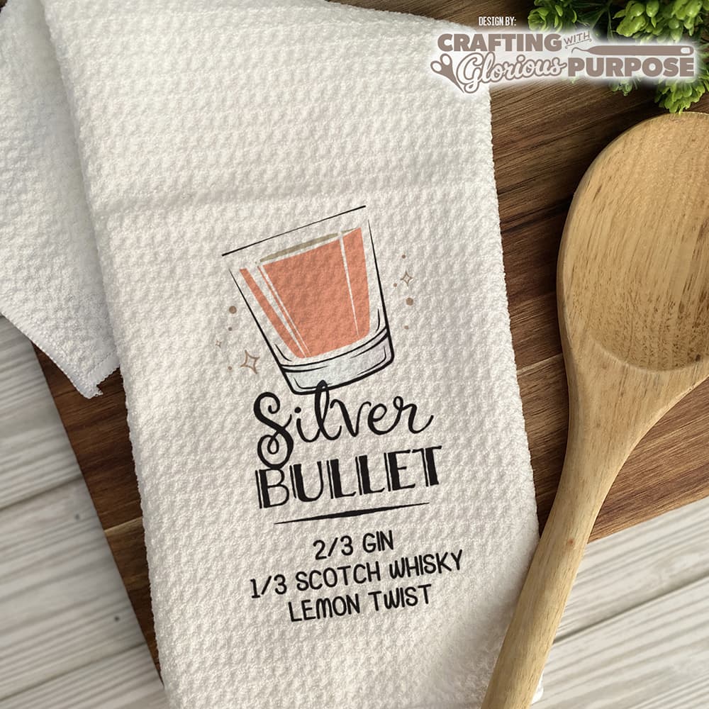 White towel with 'Silver Bullet' cocktail recipe graphic and wooden spoon on a wooden surface.