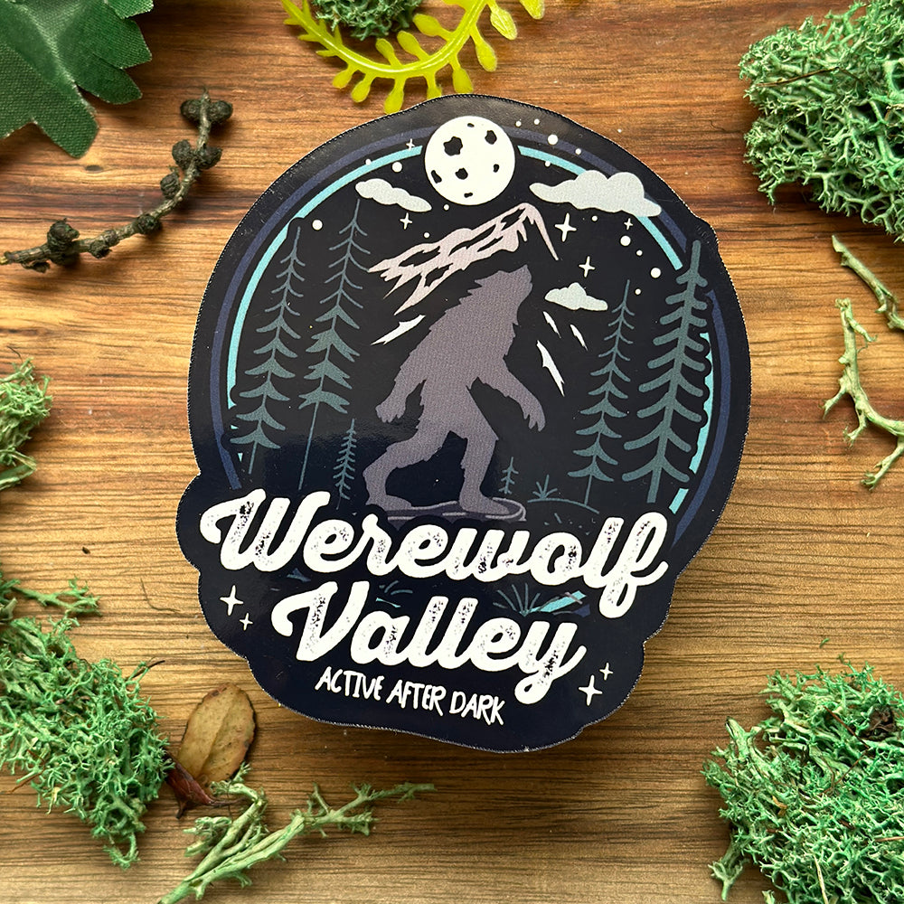 Sticker with a werewolf design and 'Werewolf Valley' text on a wooden background with greenery.