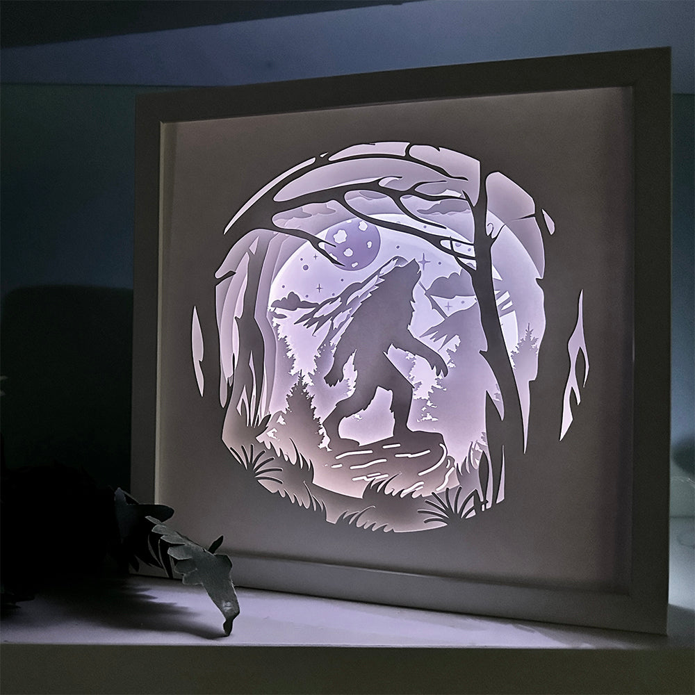 Framed paper cutout of a wolf howling at the moon in a forest setting.