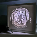 Framed paper cutout of a wolf howling at the moon in a forest setting.