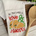 Kitchen towel with 'All you need is love & tacos' text and taco graphics on a wooden surface.